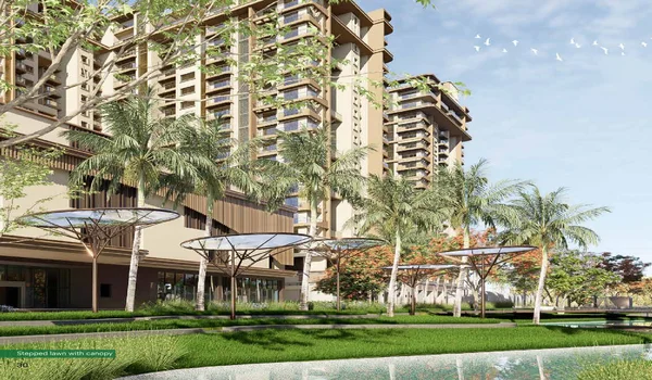 A ground-level architectural rendering of a high-rise residential tower at Sattva City. The building features contemporary balconies and a warm beige facade. In the foreground, a beautifully landscaped stepped lawn is visible, featuring modern tree-like metal canopies, lush palm trees, and a reflective water body under a clear blue sky.