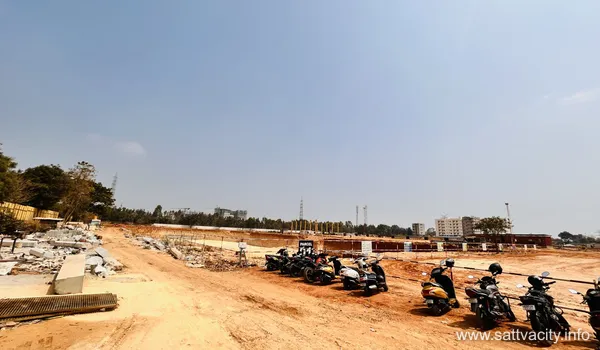 Ground-level view of the Sattva City construction project, showing a dirt access road, parked motorcycles for site staff, and leveled land plots under a clear sky.