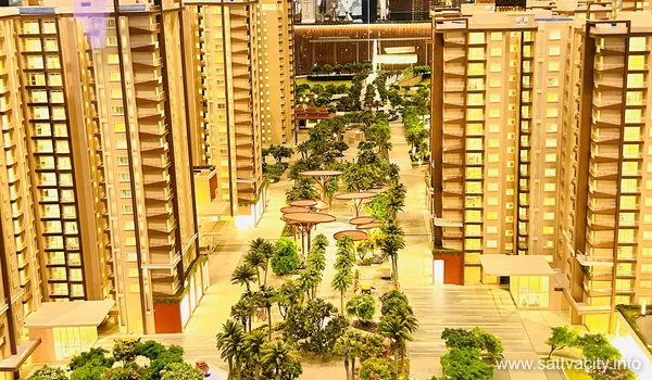 A high-angle view of a physical scale model for Sattva City, featuring two rows of glowing high-rise apartment towers flanking a lushly landscaped central promenade with miniature palm trees and circular canopy structures.