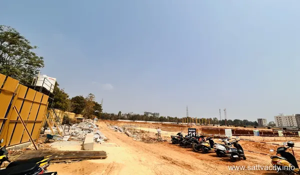 Wide-angle view of the Sattva City construction site showing cleared red earth, land parcels marked for development, and temporary site fencing under a clear blue sky.