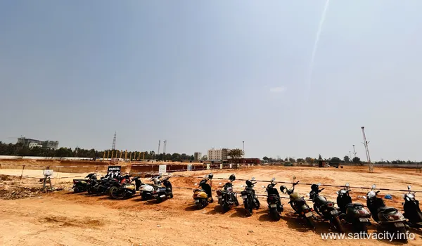 A wide-angle view of the Sattva City construction site featuring a dirt access road, organized concrete sleepers, and a line of parked scooters for site personnel, with Parcel signage indicating the demarcation of future development zones under a clear sky.